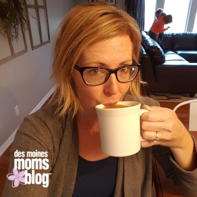 Image of blonde woman drinking coffee out of a white mug with kids fighting on the couch in the background