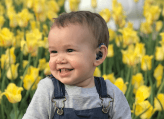 toddler sitting in front of yellow tulips with hearing aid. child deaf