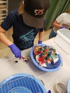 Boy with a black hat dripping colored ink on ice cubes to create an ice dye pillowcase.