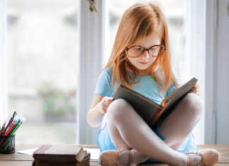 girl wearing glasses sitting on desk reading book