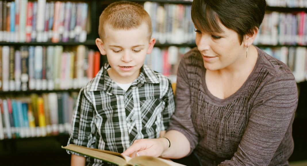 Female teacher reading to a young boy in a library.