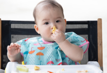 baby eating finger food in high chair. baby led weaning